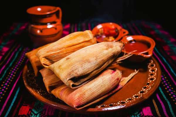 traditional Mexican tamales on a clay plate with sauce bowls on the side